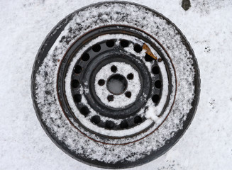 Wheel of a car covered in snow. Black wheel on snow background