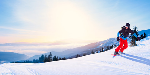 Snowboarder Riding Red Snowboard on the Slope in the Morning Mountains at Sunny Weather. Snowboarding and Winter Sports