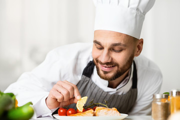 Professional Chef Guy Plating Salmon Dish Standing In Restaurant Kitchen