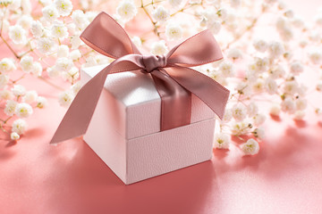 beautiful gift box with bow on pink pastel background with little aromatic flowers. Mother’s Day concept. Valentine’s Day composition.