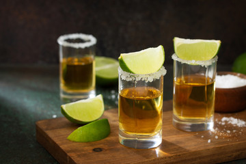Mexican Gold Tequila shot with lime and salt on dark stone background.