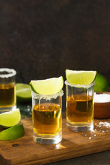 Mexican Gold Tequila shot with lime and salt on dark stone background. Copy space.
