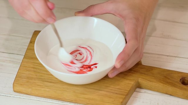 Woman whipped red color icing ream in the white bowl