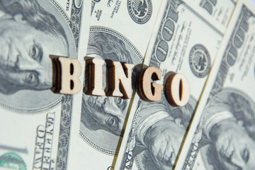 The word BINGO with wooden letters on the US dollar bills background. Top view at an angle. Selective soft focus.
