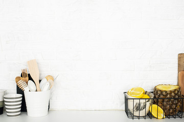 Kitchen shelf with baskets for storing products, pineapple, lemons, cutlery in a glass, chopping wooden boards on a white brick background. Style home scandi minimalism trend of modernity. Copy space,