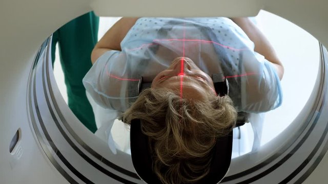 Aged female patient is undergoing MRI or CT scan under supervision of a radiologist in modern medical clinic. 4K