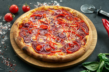 Pizza with a large number of toppings: hunting sausages, onions, salami, cheese and chilli. Pizza in composition with ingredients on a black background
