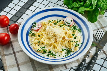 Italian fettuccine pasta in cheese sauce with parmesan, cherry tomatoes and herbs in white ceramic bowl on white background. Tasty food background