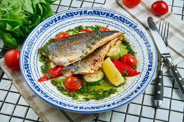 Close up view on fresh pan-fried seabass served with potato and tomato cherry in white plate. Food...