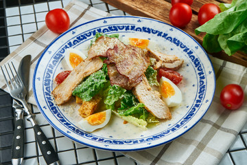 Caesar salad with croutons, parmesan, chicken, egg in a white stylish bowl. Restaurant serving. Selective focus, wooden background