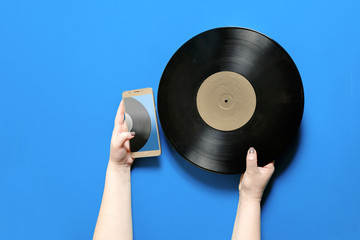 A hand holds a mobile phone near a vinyl record. Digital track list concept