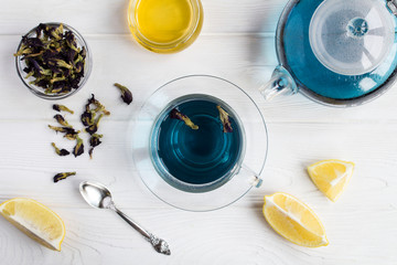 Blue flower tea in the glass cup and teapot  on  the white wooden background. Top view.