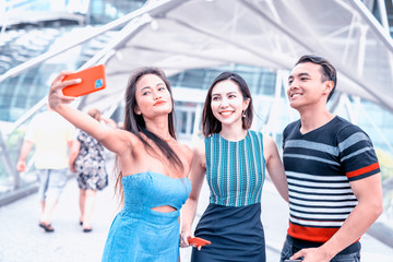 Three young asian friends walking and taking selfies around the city