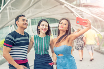 Three asian friends walking along the city taking selfies. Tourism and holiday concept