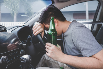 Young asian man drives a car with drunk a bottle of beer and fall asleep behind the wheel of a car