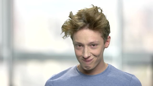 Close up teenage boy making silly face. Portrait of teenage boy grimacing on blurred background. Human funny expression.