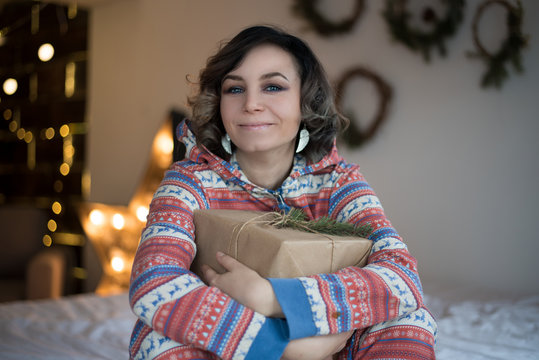 A portrait of beautiful young happy girl holding a christmas gift with a fir-tree twig.