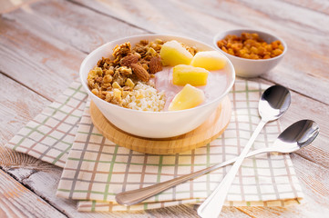 Baked granola with nuts, cottage cheese, strawberry yogurt and pineapple slices in a plate on a checkered napkin. The light of the morning sun. Healthy breakfast