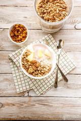 Top view baked granola with nuts, cottage cheese, strawberry yogurt and pineapple slices in a plate on a checkered napkin. The light of the morning sun. Healthy breakfast