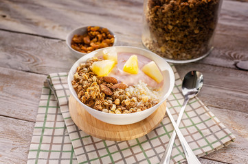 Close up baked granola with nuts, cottage cheese, strawberry yogurt and pineapple slices in a plate on a checkered napkin. The light of the morning sun. Healthy breakfast