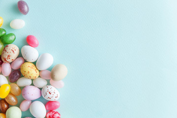 Happy Easter concept. Preparation for holiday. Easter candy chocolate eggs and jellybean sweets isolated on trendy pastel blue background. Simple minimalism flat lay top view copy space.