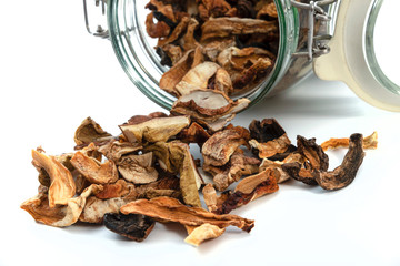 Close-up of dried homemade mushrooms poured out of a vintage glass jar on a white background.
