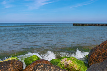 The big stones and wooden breakwaters protect the coast of the Baltic Sea. Landscape on a sunny summer day. City Pionersky, Kaliningrad region