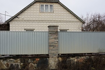 part of a long gray fence of metal and stones on the street in front of a rural brick house