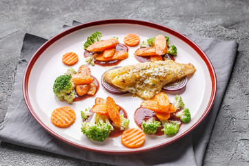 Fillet of sea bass with vegetables. Baked fish, cauliflower and carrots on a big plate. Gray background