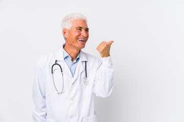 Mature caucasian doctor man points with thumb finger away, laughing and carefree.