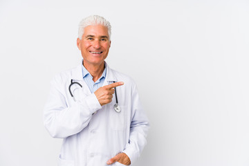Mature caucasian doctor man smiling and pointing aside, showing something at blank space.