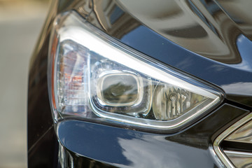 Headlamp of a car parked near curb on the side of the street on a parking lot.