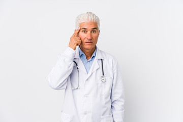 Mature caucasian doctor man pointing temple with finger, thinking, focused on a task.