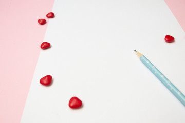 A white note and a blue pencil with red hearts on pink background