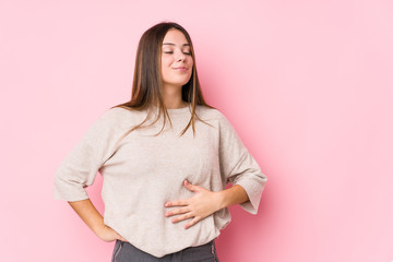 Young caucasian woman posing isolated touches tummy, smiles gently, eating and satisfaction concept.