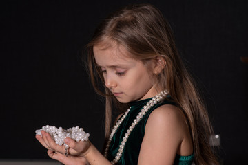 Portrait of a beautiful little girl with a beads on a dark background.