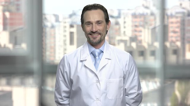 Portrait of attractive man in white coat. Handsome middle-aged researcher smiling and looking at camera. Blurred urban background.