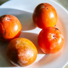 Persimmon fruits on a white plate close-up top view.