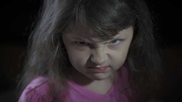 Portrait of an angry kid. Angry little girl on a black background.