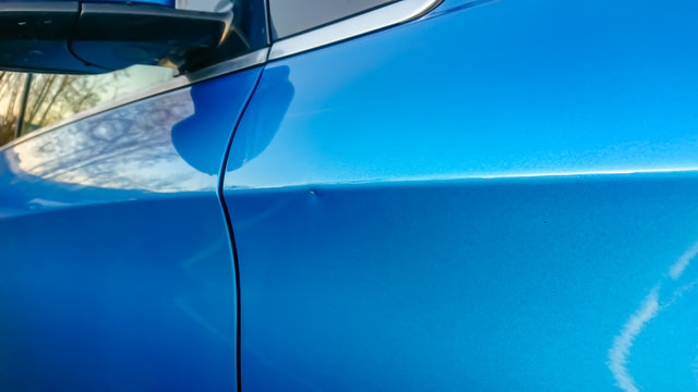 A small dent in the fender of a blue metallic European car