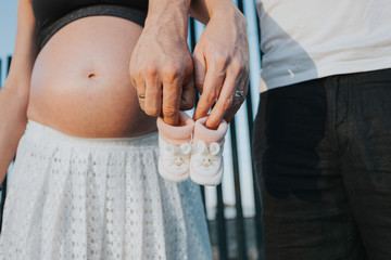 Obraz na płótnie Canvas Expecting parents holding little baby boy shoes