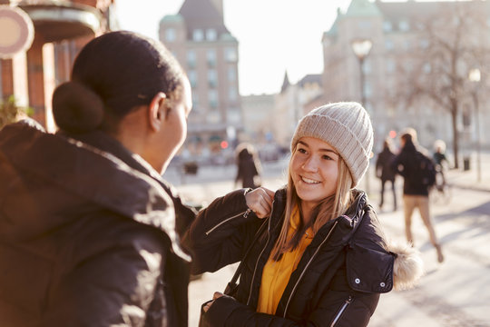 Smiling teenage girl talking to friend in city during winter