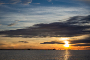 A pier on the Mediterranean Sea in Tuscany at sunset with an island and a sailboat in the background