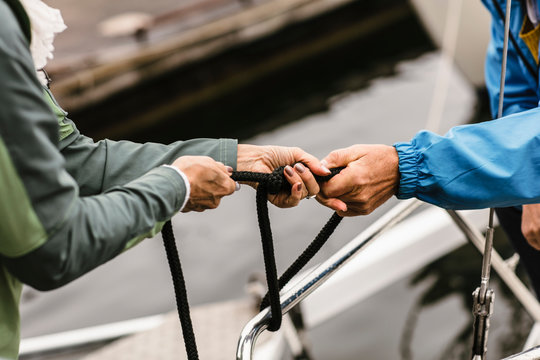 Cropped hands of female instructor and senior man tying rope on yacht's railing