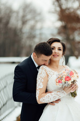 Winter photo shoot newlyweds. Young girl bride with a bouquet. Beautiful wedding couple. Winter wedding of the groom in a beautiful suit and the bride in a beautiful wedding dress.