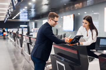 Business trip. Handsome young businessman in suit holding his passport and talking to woman at airline check in counter in the airport - 314150765