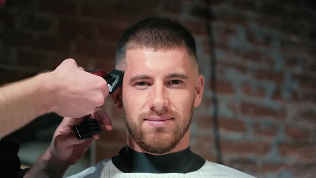 Close-up view on male's hairstyling in a barber shop with professional trimmer. Man's haircutting at hair salon with electric clipper. Grooming the hair. Slow motion.
