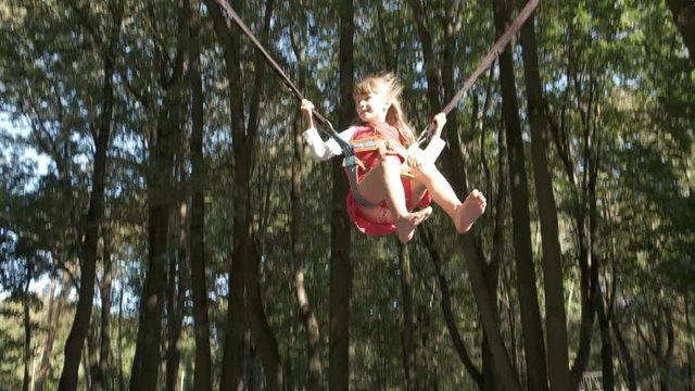 Child girl jumping fastened on a trampoline in summer park.