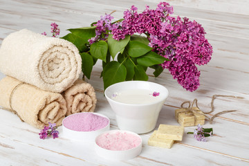 Spa and bath cosmetics with lilac flowers. Bath salt, soap, cream, oil, milk, serum and towel rolls on wooden rustic background. Organic natural cosmetic. Fresh care of body. Eco lifestyle