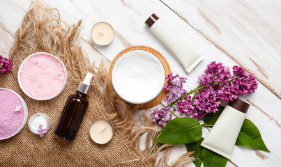 Spa and bath cosmetics with lilac flowers. Bath salt, soap, cream, oil, milk, serum and towel rolls on wooden rustic background. Organic natural cosmetic. Fresh care of body. Eco lifestyle